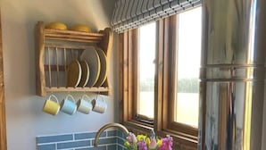 A kitchen with a double sink, a window with curtains, a shelf with plates, and a refrigerator. - Shepherd Hut in Private Meadow With Outdoor Bath (Langport)