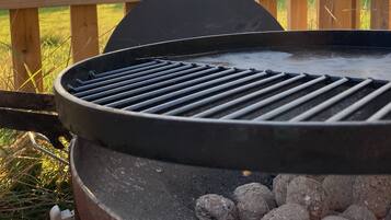 A barbecue grill with charcoal, a wooden fence, and a cloudy sky in the background.