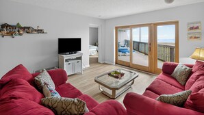Una sala de estar con un sofá rojo, una mesa de centro de vidrio, un televisor de pantalla plana y un balcón con vistas.