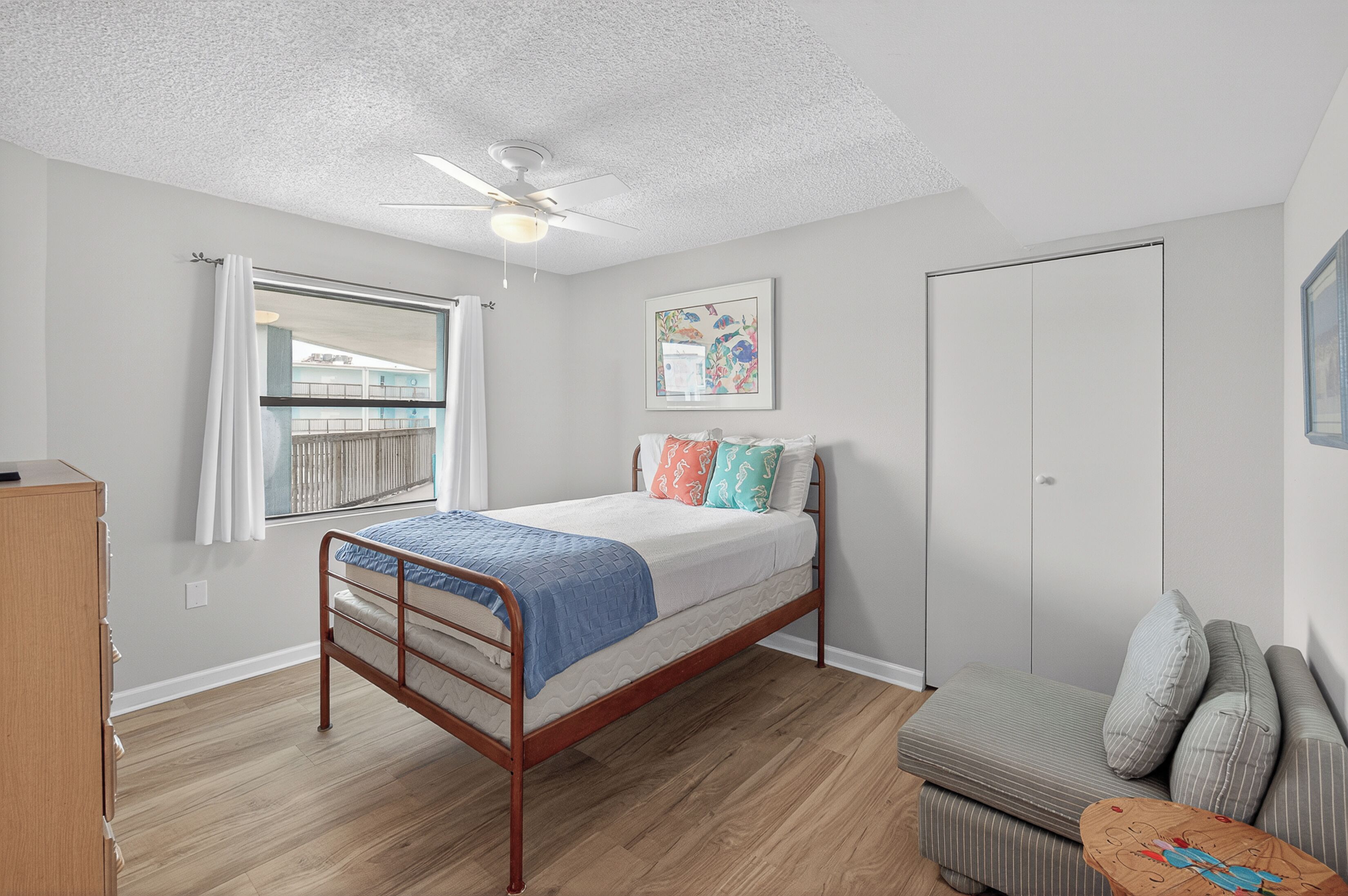 A bedroom with a bed, a window with curtains, a ceiling fan, a wardrobe, and a sofa.