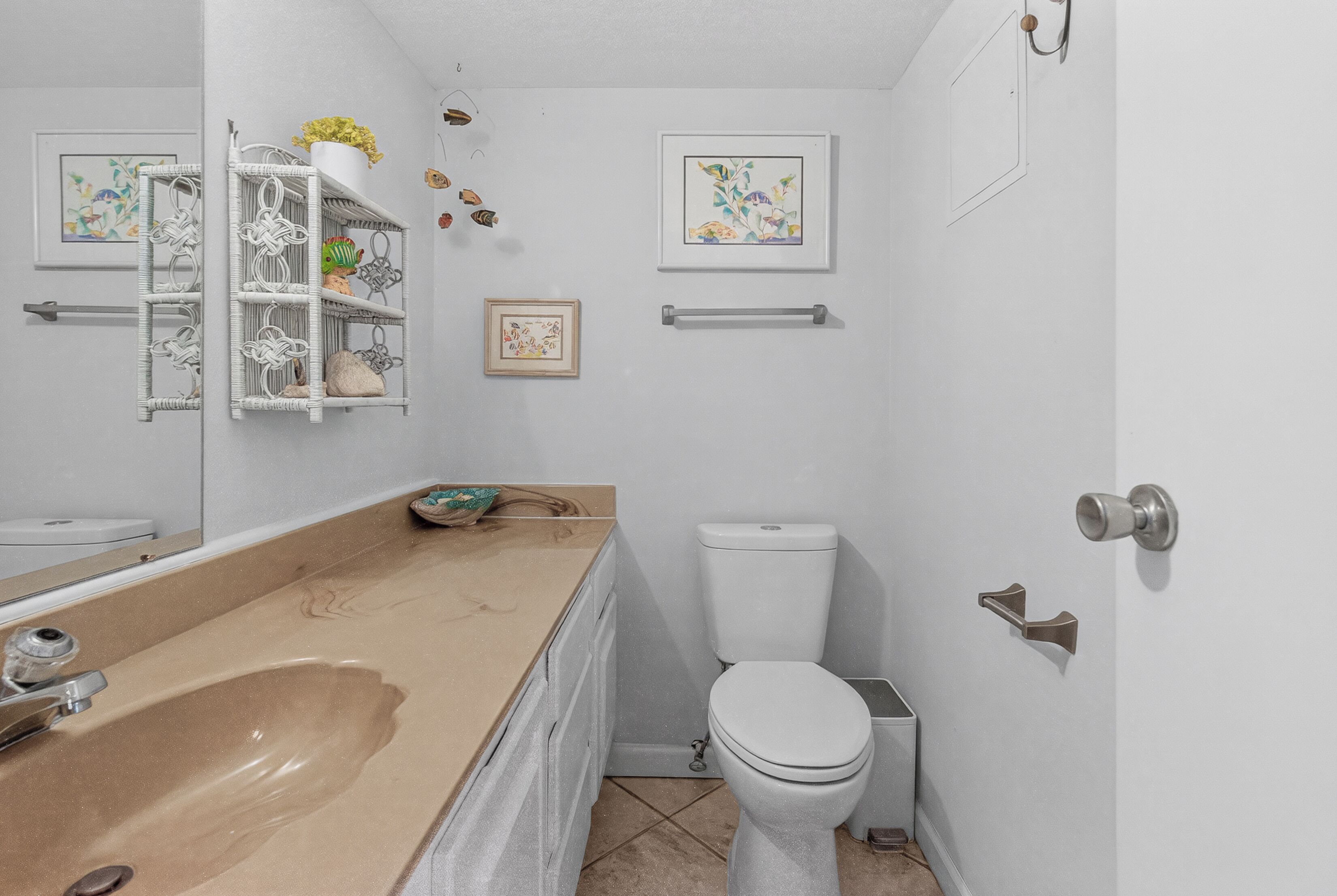 Et badeværelse med en beige vask, et hvidt toilet og en hvid hylde med pynt.