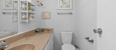Et badeværelse med en beige vask, et hvidt toilet og en hvid hylde med pynt.