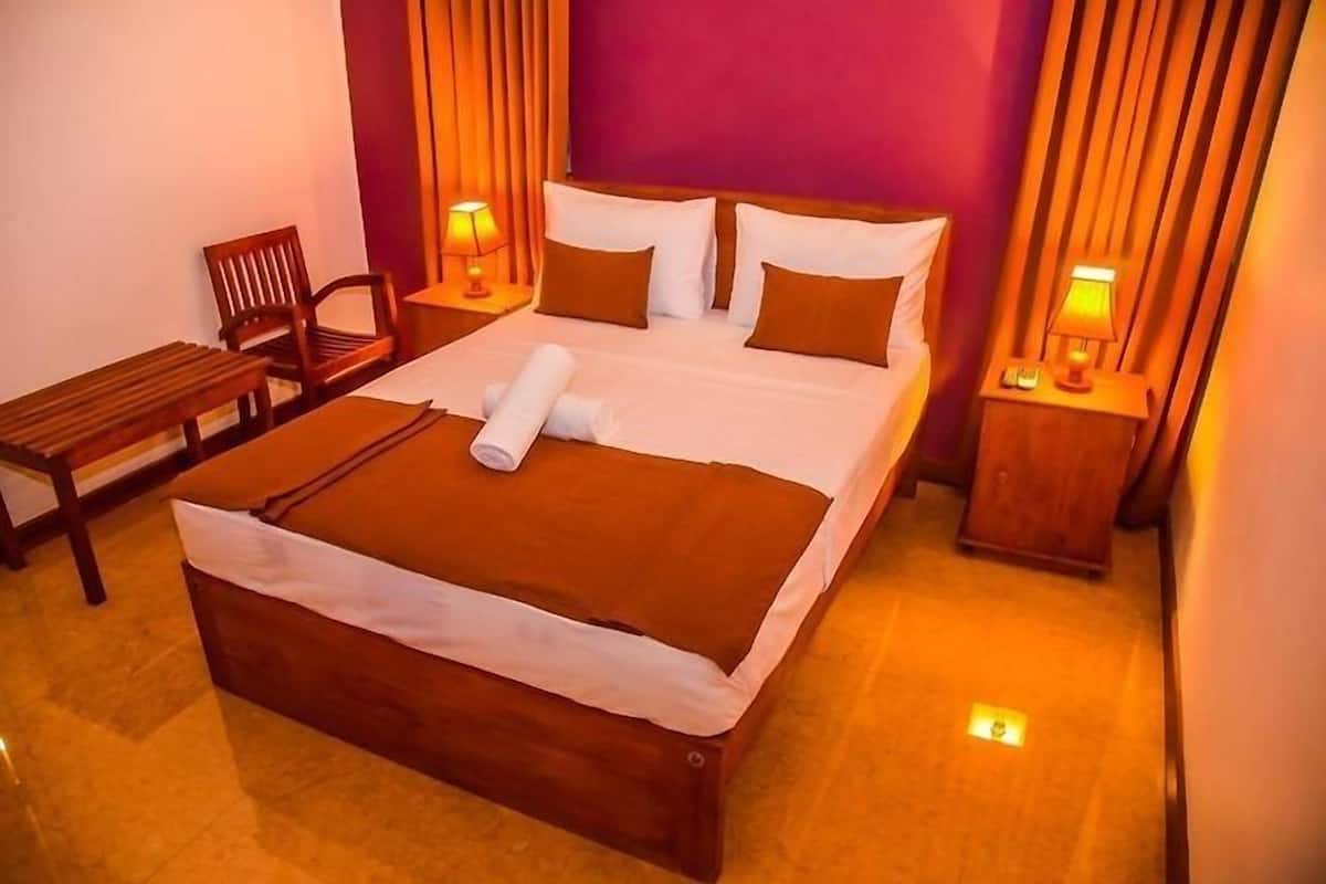 A neatly made bed with a brown blanket and pillows, two bedside lamps, a wooden chair, and a small table.
