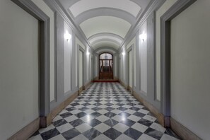 Un couloir avec un sol à carreaux, des murs blancs et une porte en bois au fond.