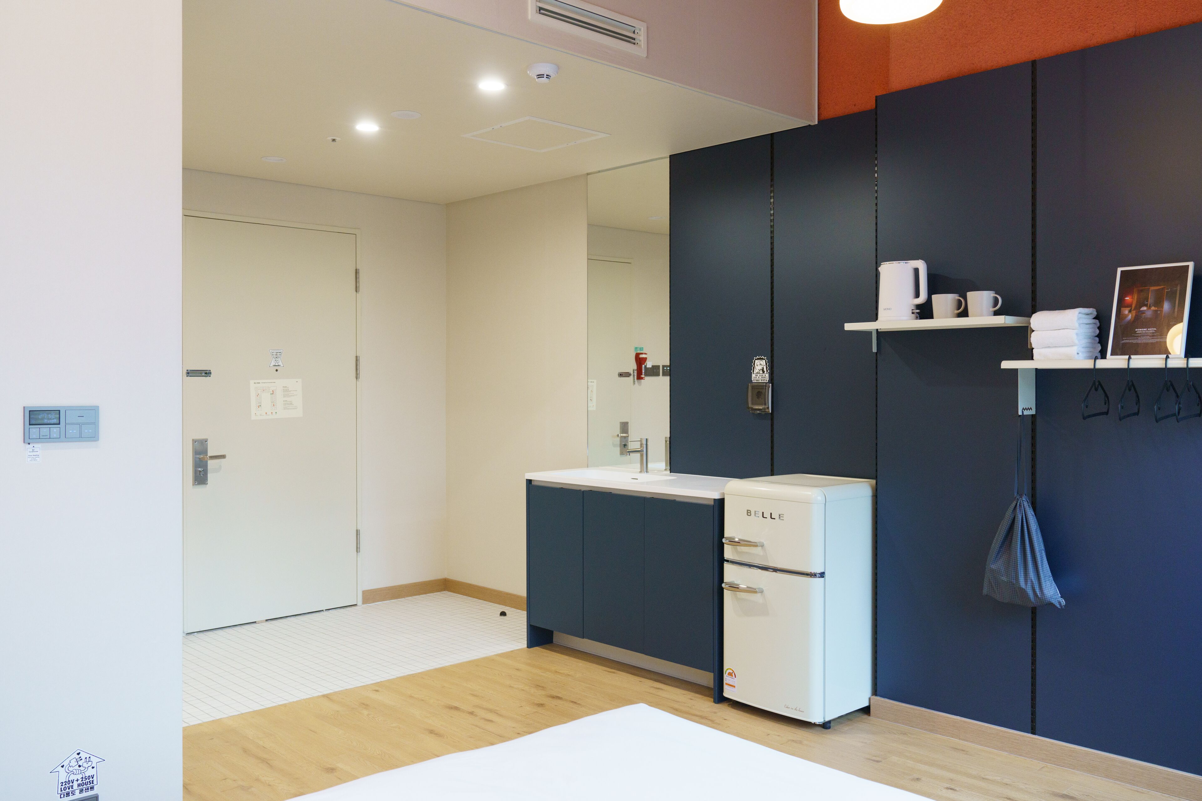 A modern bathroom with a white sink, dark blue cabinets, and a mirror. There is a white heater, a towel rack, and a shelf with toiletries.