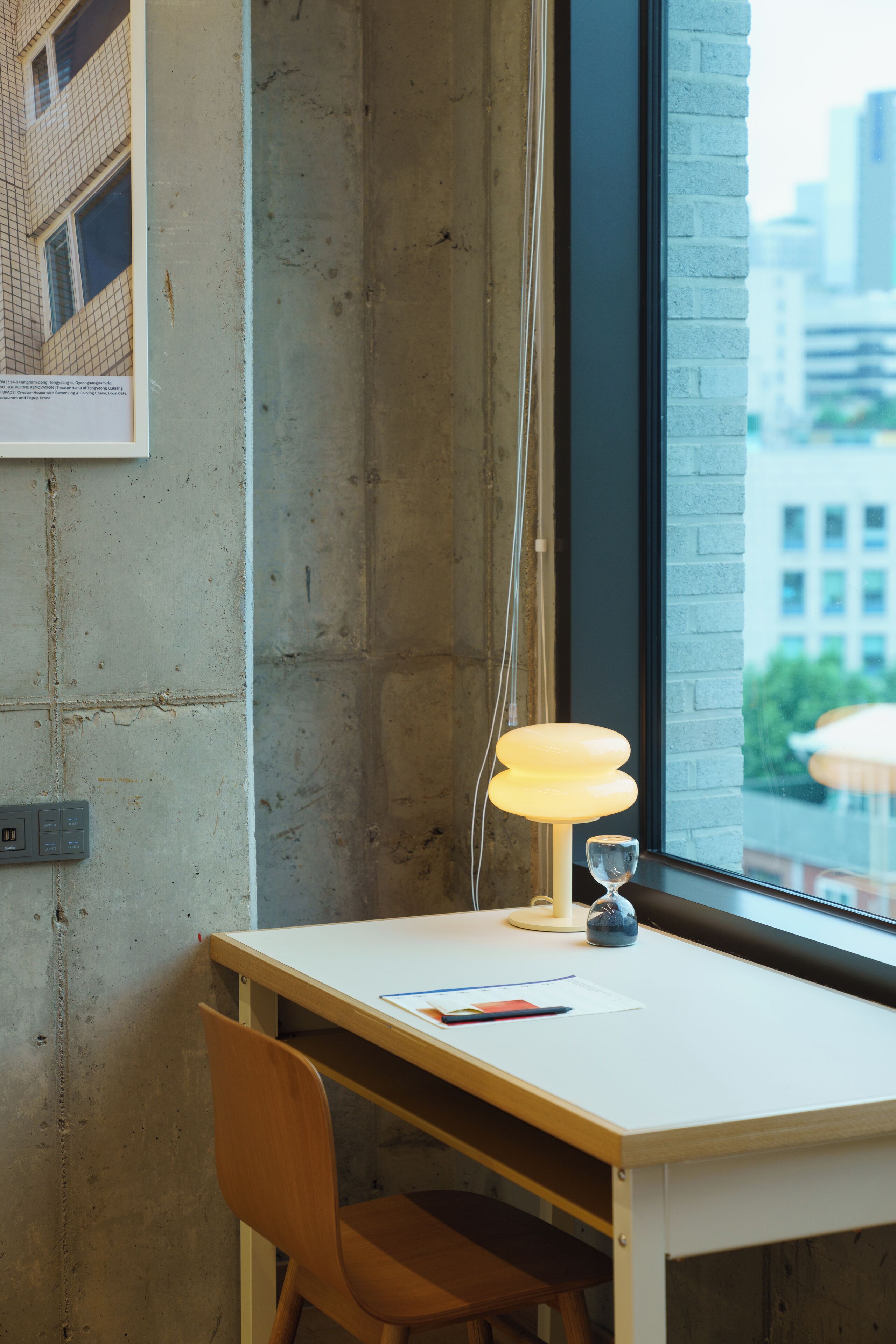 Un espacio de trabajo con escritorio, silla, lámpara y ventana que ofrece vistas a edificios.