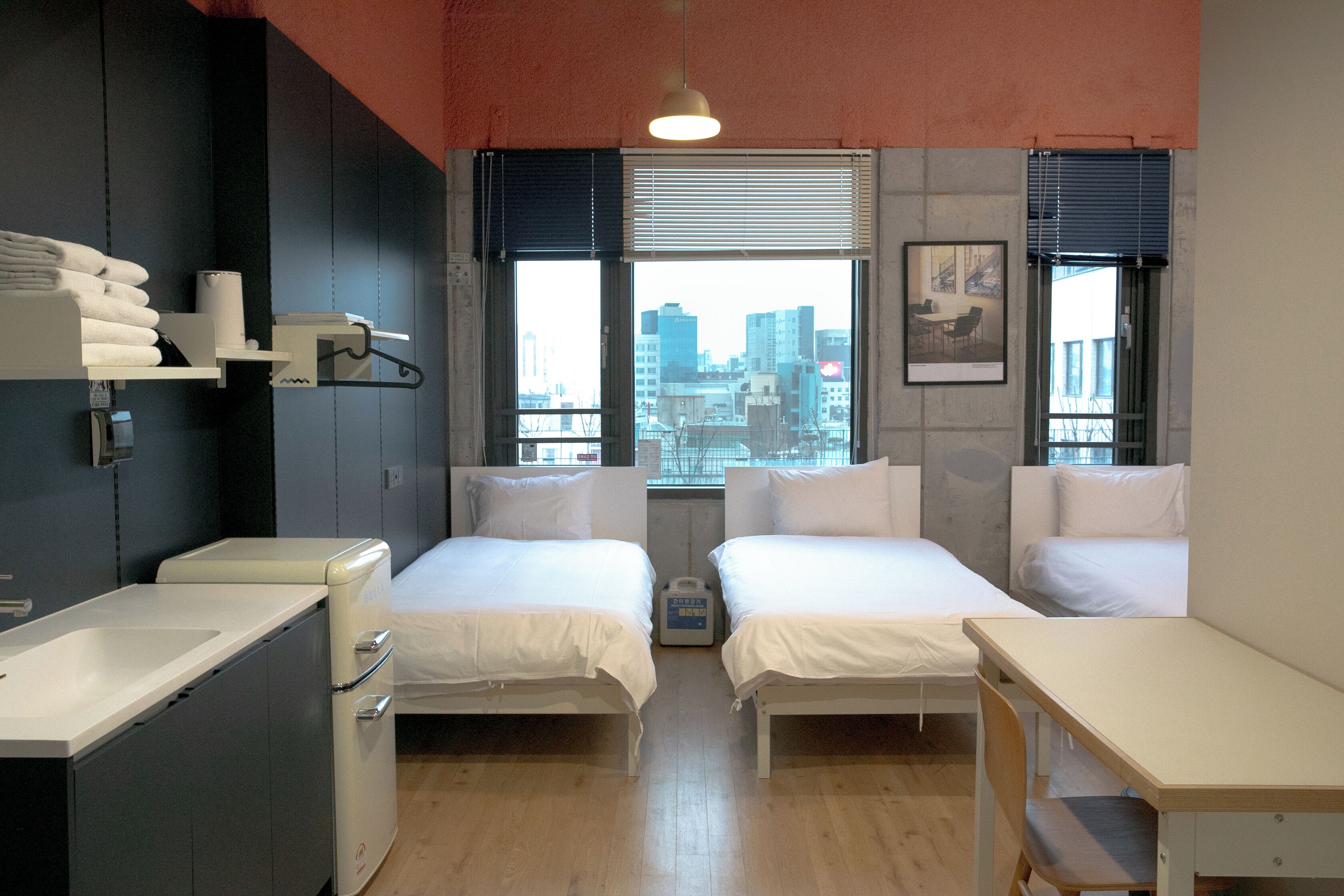 Una habitación de hotel moderna con dos camas, una kitchenette pequeña y vistas a la ciudad.
