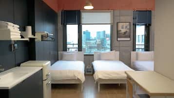 Una habitación de hotel moderna con dos camas, una kitchenette pequeña y vistas a la ciudad.