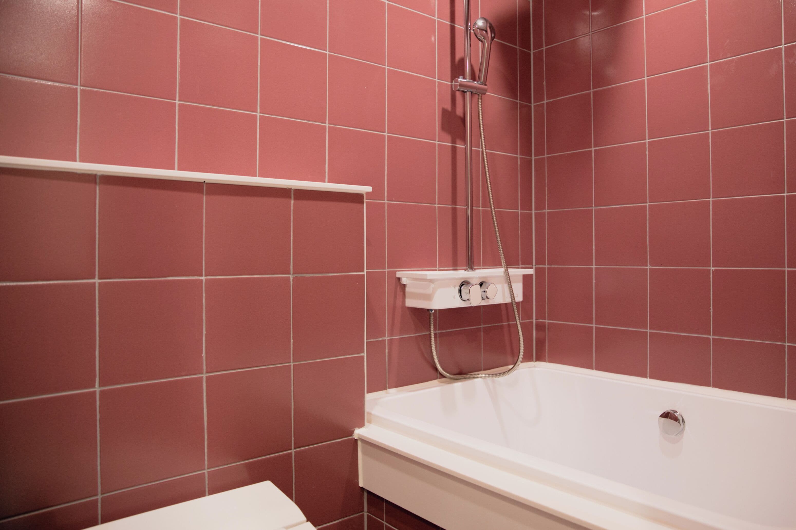 Un baño con una bañera blanca y una ducha, frente a una pared de azulejos rojos.