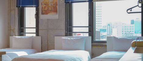 Habitación de hotel con dos camas, una ventana con persianas, un cartel en la pared y vistas a la ciudad.