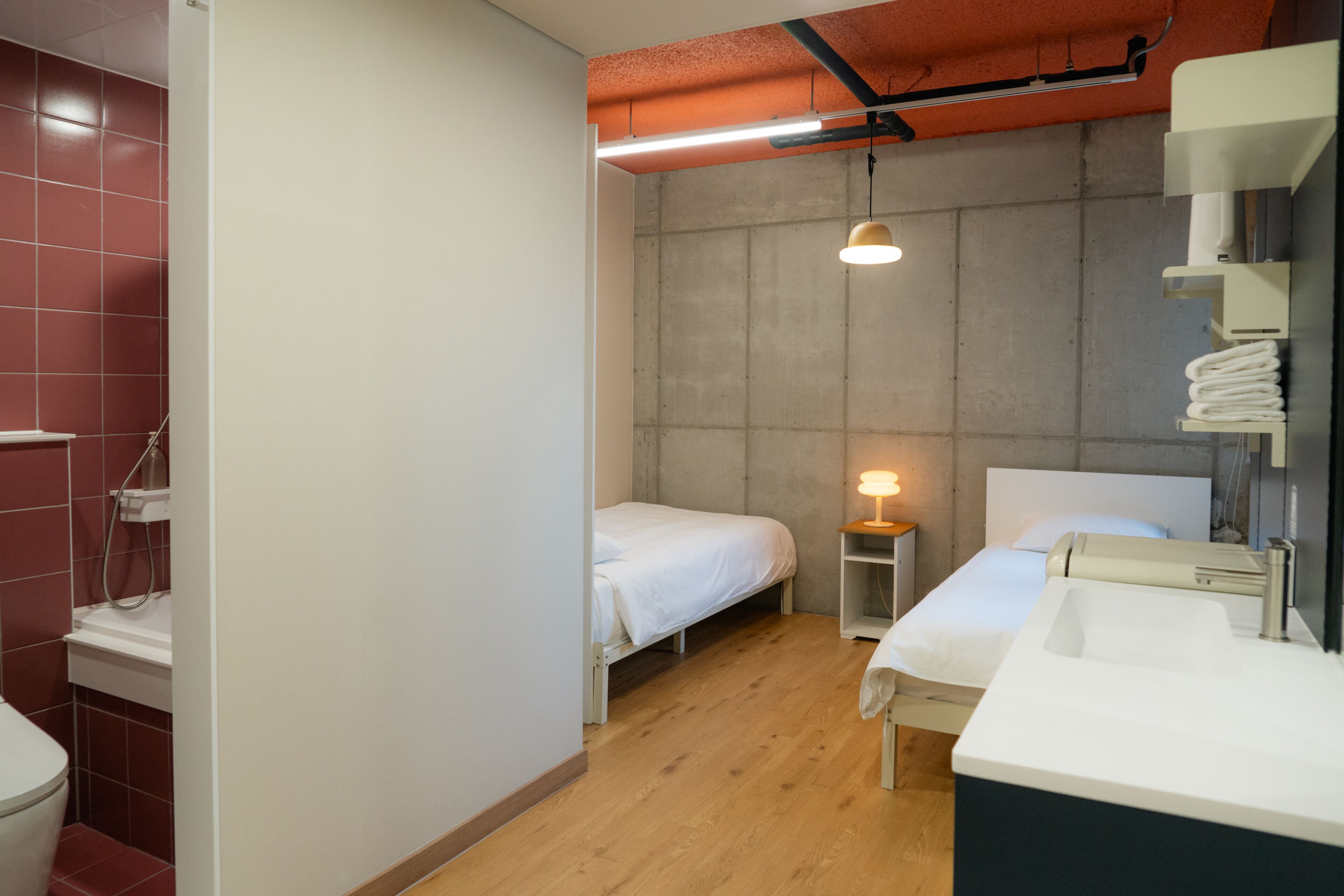 A compact hotel room with a single bed, a bedside table with a lamp, a built-in sink, and a shower area.