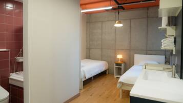 A compact hotel room with a single bed, a bedside table with a lamp, a built-in sink, and a shower area.