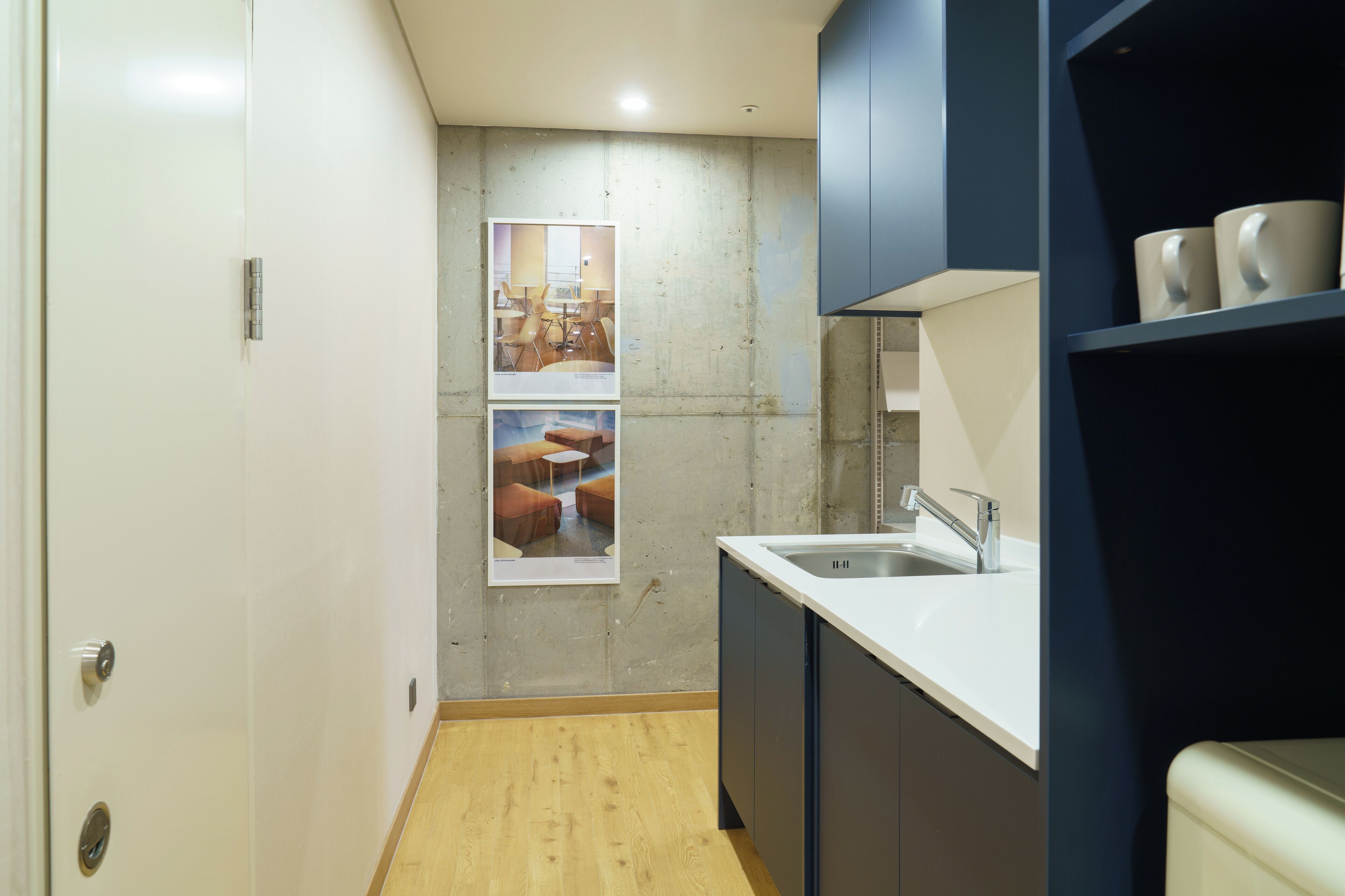 A narrow kitchen with a wooden floor, a white sink, and dark cabinets.