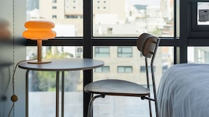 Une chambre d’hôtel moderne avec une grande fenêtre, une table ronde avec une lampe, une chaise et un lit.
