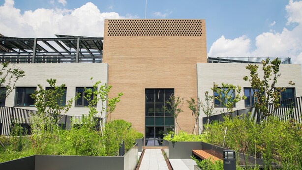Un bâtiment moderne avec une entrée centrale, entouré de verdure et de bancs.