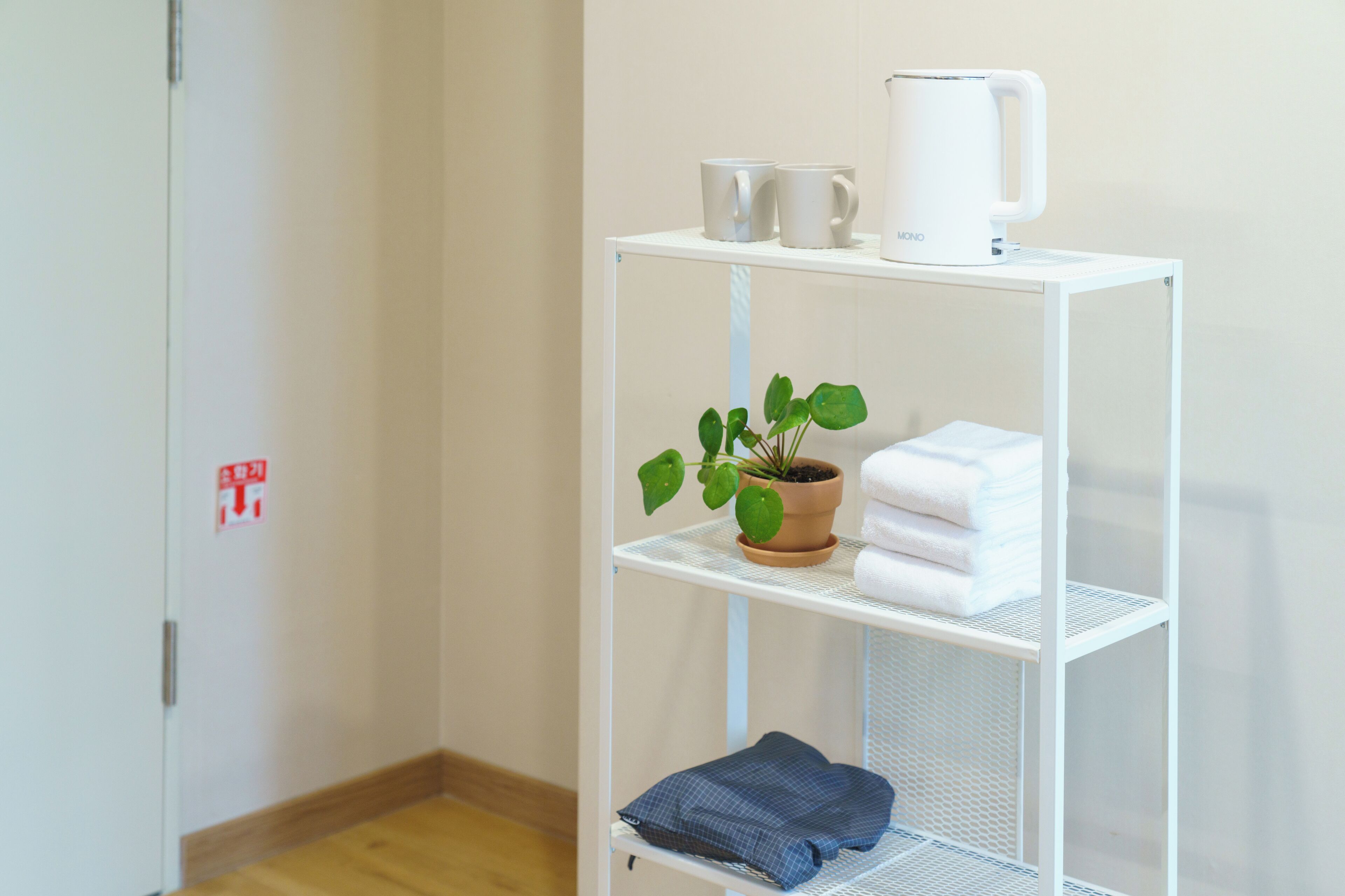 A white metal shelf with a potted plant, a white kettle, and folded towels.