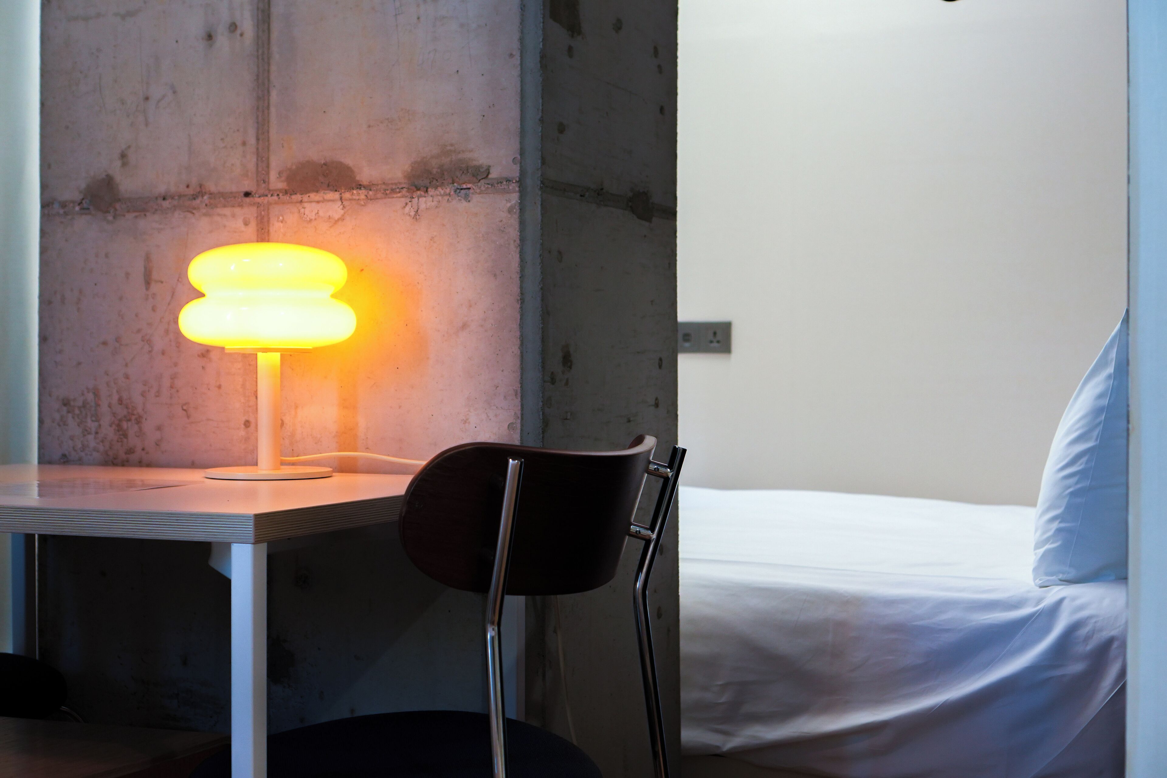 Una habitación con cama, una silla, una mesa y una lámpara.