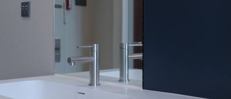 A modern bathroom with a white sink, chrome faucet, and a large mirror.