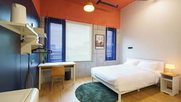 Une chambre à coucher comprenant un lit, une table de chevet, un bureau, une chaise et une fenêtre avec des stores.