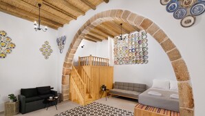 A room with a wooden staircase, a bed with a grey duvet, a black sofa, and a patterned rug. - Antica Casa Dei Nonni (Rhodes)