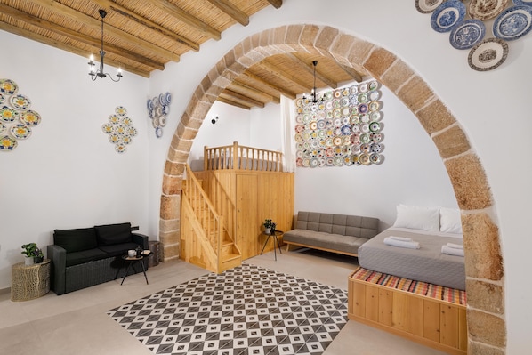 A room with a wooden staircase, a bed with a grey duvet, a black sofa, and a patterned rug. - Antica Casa Dei Nonni (Rhodes)