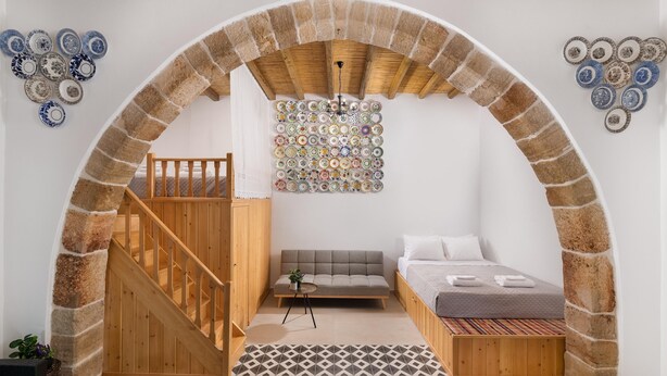 A cozy room with a wooden staircase, a sofa, a bed, and a wall decorated with plates. - Antica Casa Dei Nonni (Rhodes)