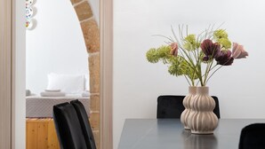A dining area with a table and chairs, a vase with flowers, and a view of a bed and a brick wall. - Antica Casa Dei Nonni (Rhodes)