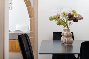 A dining area with a table and chairs, a vase with flowers, and a view of a bed and a brick wall. - Antica Casa Dei Nonni (Rhodes)