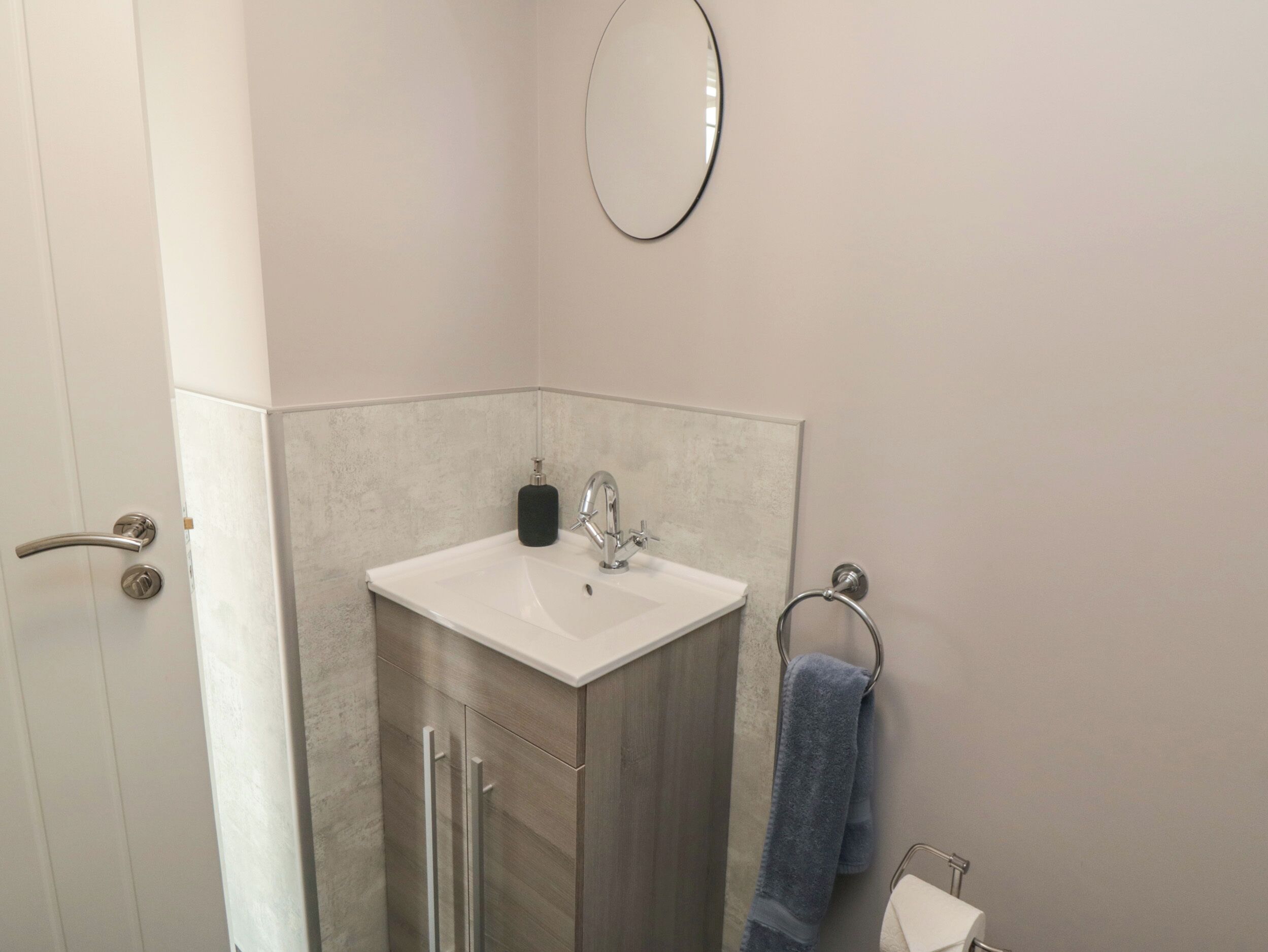 Un baño con lavamanos blanco, un espejo, toallero y una puerta.