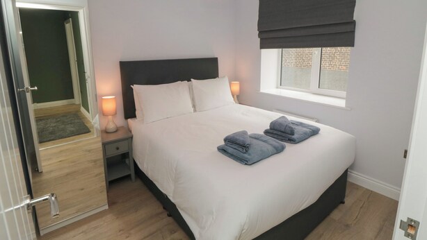 A bedroom with a bed, bedside lamps, a window with a view, and a door leading to another room. - 1 Staveley Cottages (Driffield)