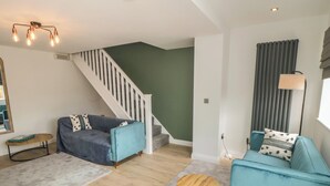 A modern living room with a staircase, two sofas, a coffee table, and a lamp. - 1 Staveley Cottages (Driffield)