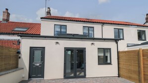 A two-story house with a red-tiled roof, a small patio area with brick flooring, and a black door. - 1 Staveley Cottages (Driffield)