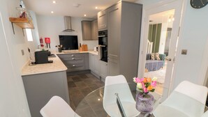 A modern kitchen with grey cabinets, a central island, and a dining area with a glass table and white chairs. - 1 Staveley Cottages (Driffield)