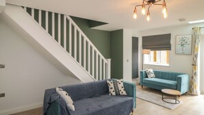 A modern living room with a blue sofa, a wooden coffee table, and a staircase with white railings. - 1 Staveley Cottages (Driffield)