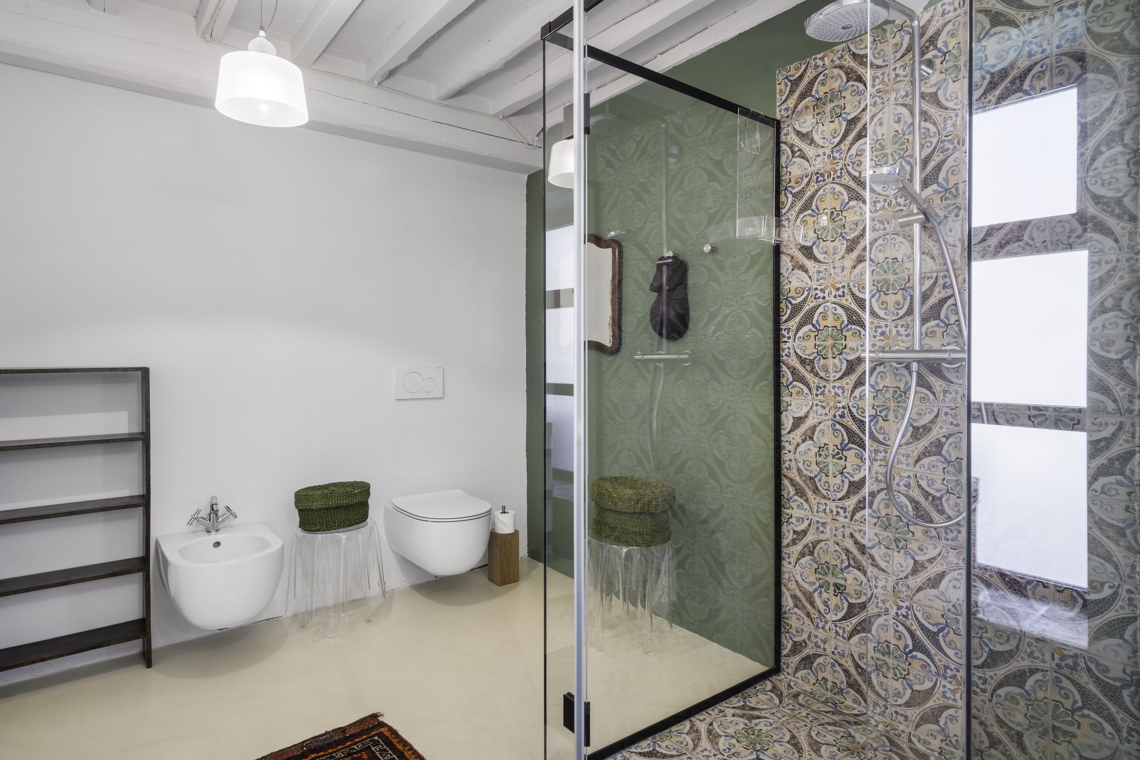 A modern bathroom with a glass shower enclosure, a white sink, a toilet, and a decorative wall with patterned tiles.