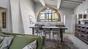 Ein großzügiger Wohnbereich mit einem grünen Sofa, einem Esstisch mit Stühlen, einer Küche und einem großen Fenster sowie einem Kühlschrank.