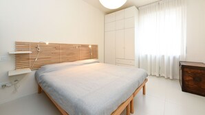 Ein modernes Schlafzimmer mit einem Holz-Kopfteil, einem Bett mit grauer Bettdecke, einem Kleiderschrank und einem Nachttisch.