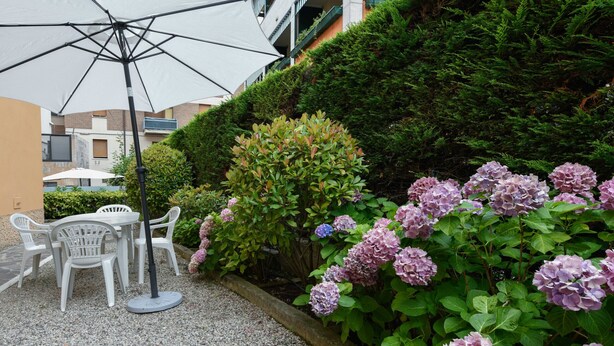 Ein Sitzbereich im Freien mit Tisch und Stühlen, umgeben von einer Hecke und Hortensienblüten.