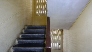 A staircase with dark steps and a wooden handrail, leading to a landing with a textured wall and a ceiling with a grid pattern. - Hotel Dream inn (Mumbai)