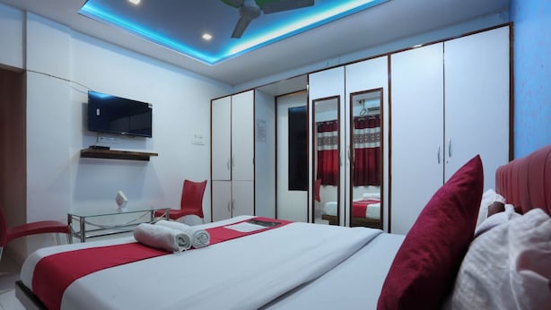 A hotel room with a bed, a TV mounted on the wall, a wardrobe, and a ceiling fan. - Hotel Dream inn (Mumbai)