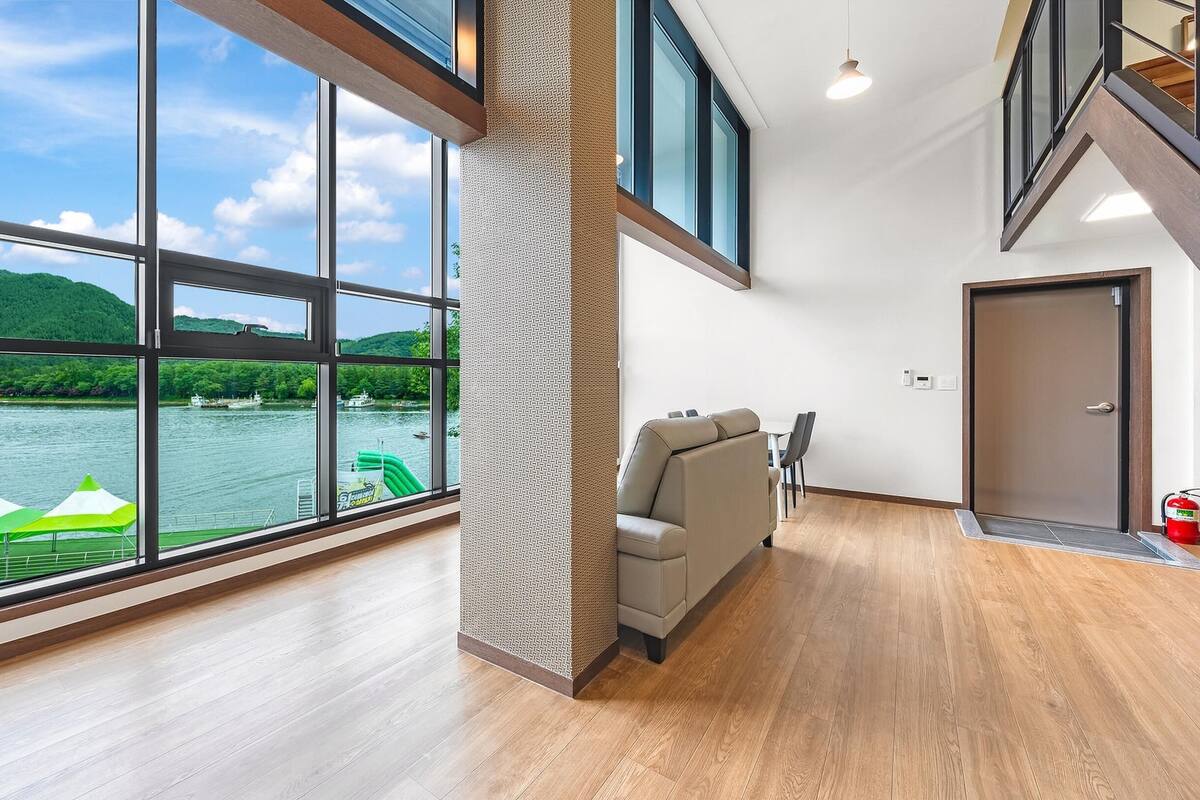 Amplia habitación con grandes ventanales que dan a un lago y colinas.