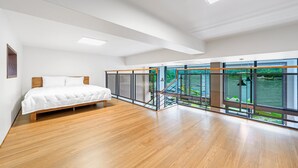 Un dormitorio amplio con una cama grande, piso de madera y vista a una masa de agua a través de amplias ventanas.