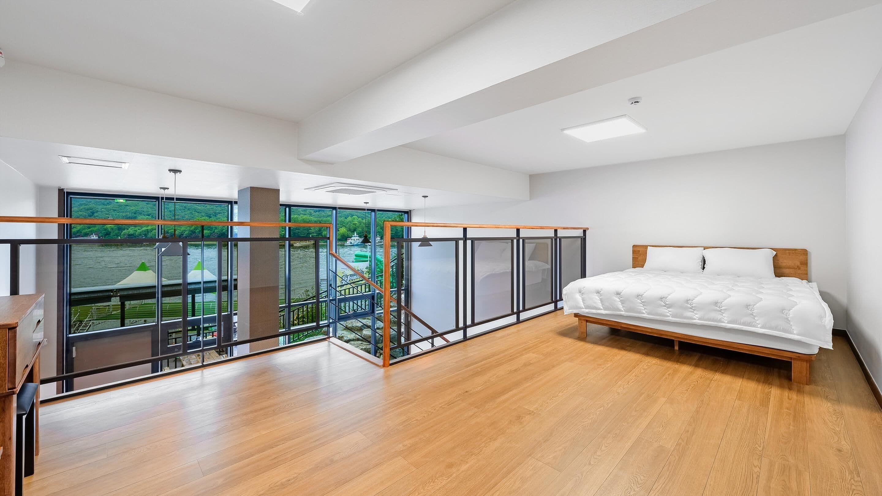 A bedroom with a wooden bed, a glass partition, and a view of a water body.