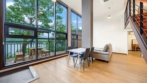 Amplia habitación con grandes ventanales que ofrecen vistas a un lago, una mesa de comedor de madera con sillas, un sofá y una escalera.