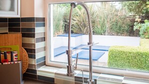 A kitchen with a modern faucet, a window with a view of greenery, and a tiled backsplash. - Rugby Lodge 3 Bedrooms Dublin (Dublin)
