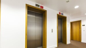 A hallway with two elevators, carpeted floor, and wooden doors. - Grande Central Sandyford (Dublin)