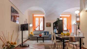 Un ambiente compatto con divano, tavolo da pranzo, sedie, televisore e libreria.