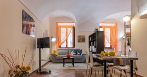 A compact living space with a sofa, dining table, and chairs, a TV, and a bookshelf.