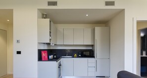 A modern kitchen with white cabinets, a black countertop, and a microwave. There is a red sign on the wall and a grey sofa in the foreground. - Riviera Flavour Apartments by Wonderful Italy - Lavanda (Santa Margherita Ligure)