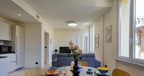 A modern kitchen with white cabinets, a dining area with a round table set for four, and a living room with a sofa and a TV. - Riviera Flavour Apartments by Wonderful Italy - Lavanda (Santa Margherita Ligure)